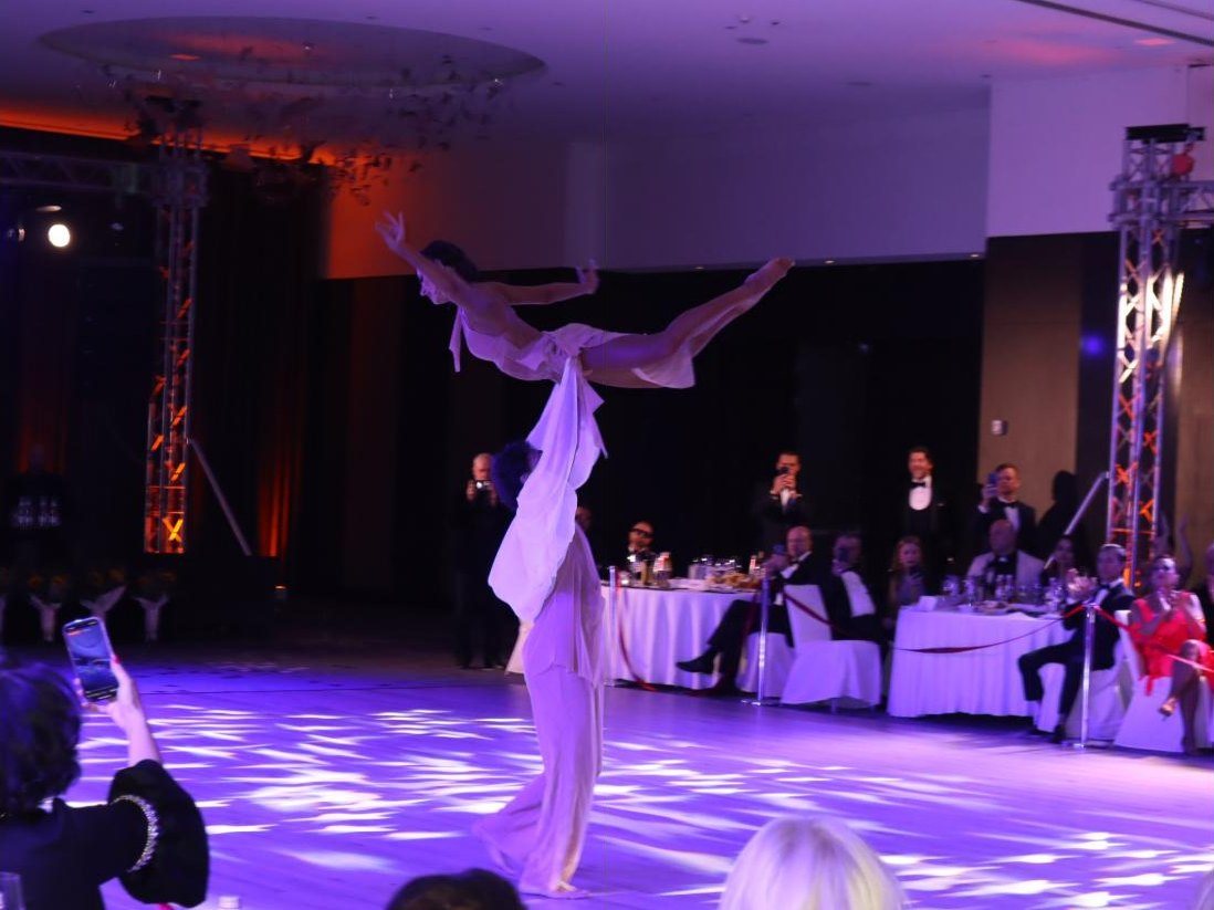 A showcase lift under violet light at the 2026 gala, guests watching from their tables
